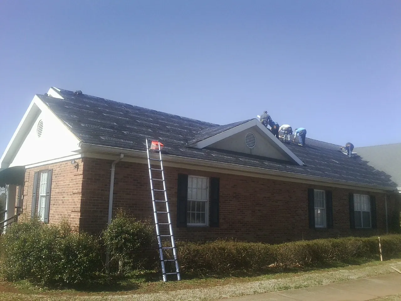 Crew tearing shingles off a brick ranch roof with a ladder set — Metal Roof Repair work by our crew in Lairdsville