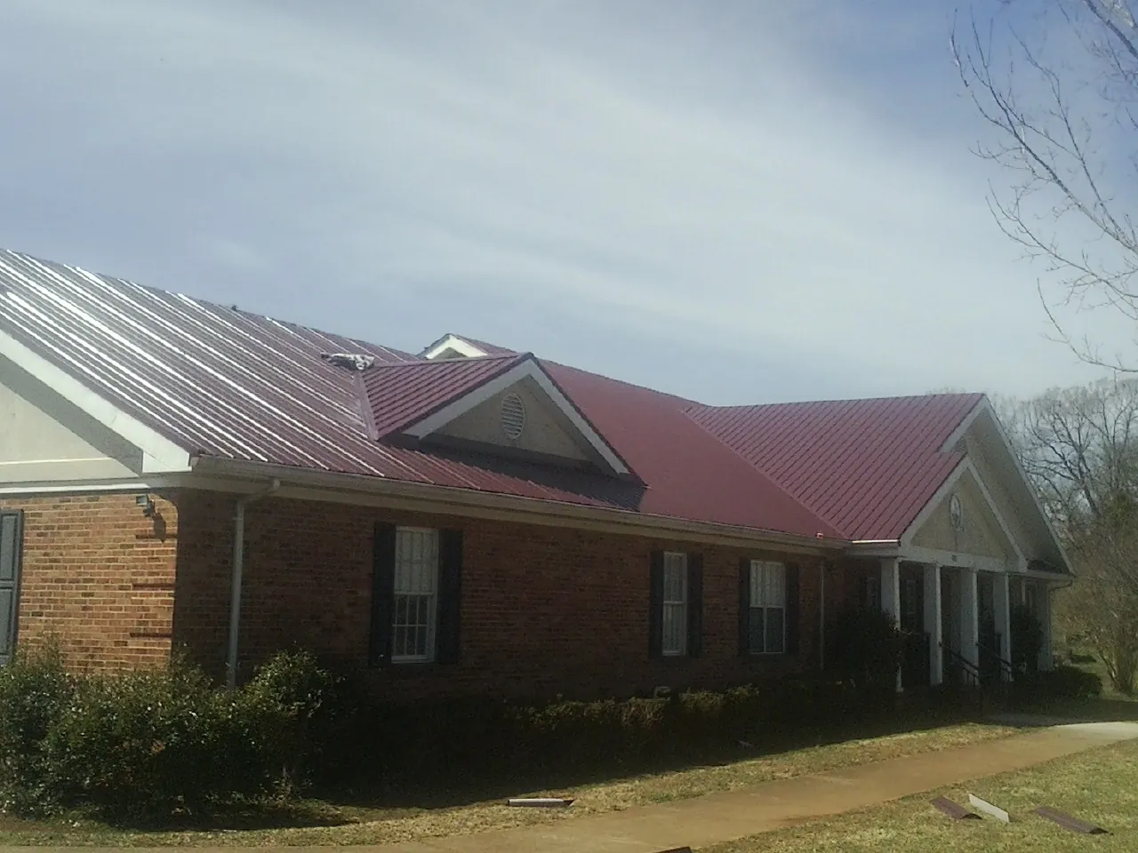 Red metal roof with gabled entries on a long brick building, from a Hail Damage Roof Repair job in Lairdsville