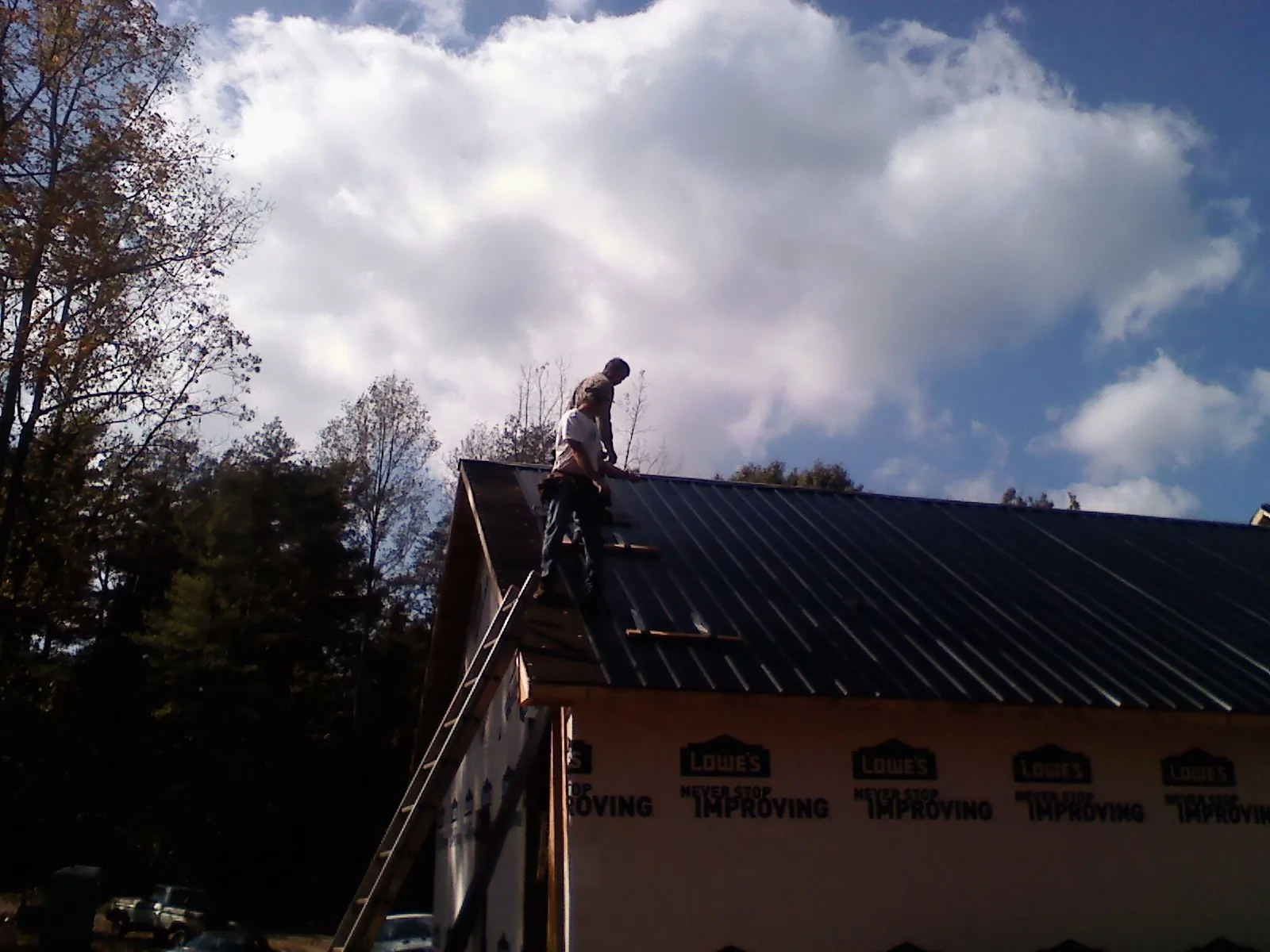 Roofer fastening dark metal panels high against a cloudy sky, from a Roof Inspection job in Lairdsville