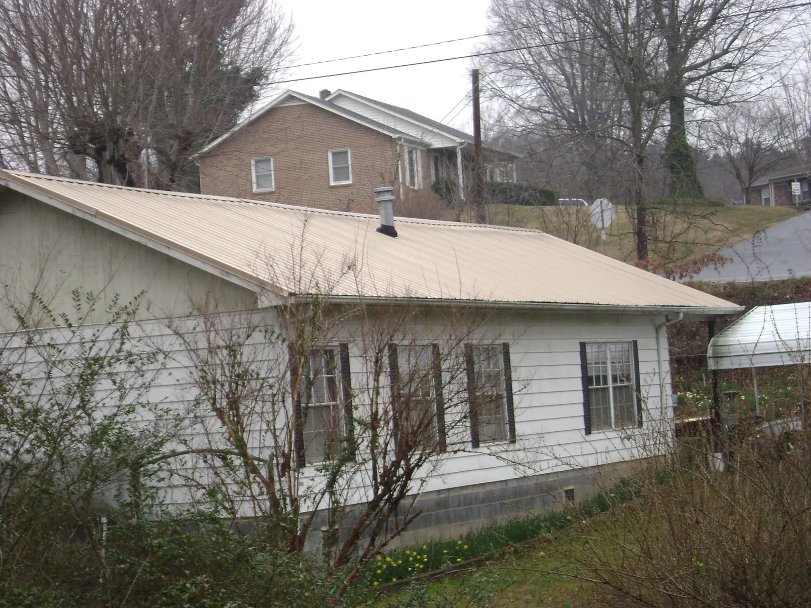 Tan metal roof on a white sided house set into a hillside — Commercial Roofing by Roofing Brothers in Lairdsville