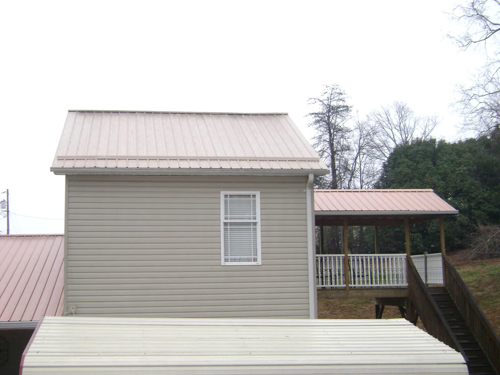 Tan metal roofs on a two story addition and attached porch, from a Roof Replacement job in Lairdsville